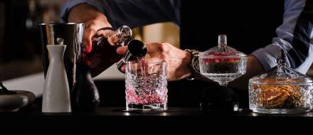Bartender versant un cocktail rose dans un verre à whisky taillé sur comptoir sombre – Boterzing Douai