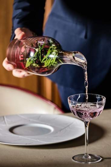 Service d'un cocktail violet aux herbes fraîches versé dans une coupe à table – Boterzing Douai