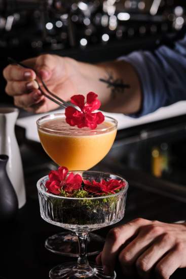 Bartender déposant des pétales de fleurs rouges sur un cocktail doré en coupe – Boterzing Douai