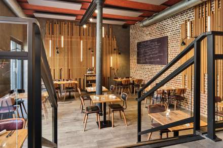 Salle du restaurant avec murs en briques, tables en bois et escalier métallique – Boterzing Douai
