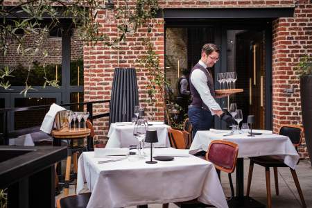Serveur dressant les tables en terrasse intérieure pavée, chaises en cuir et mur en briques – Restaurant avec terrasse Douai