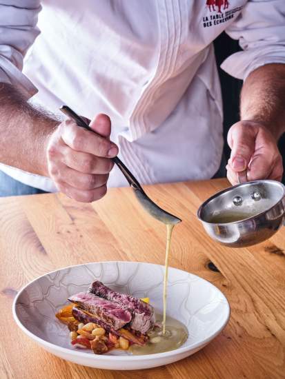 Chef nappant une pièce de viande en assiette blanche avec une cuillère, dressage en salle – La Table des Échevins Douai