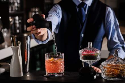 Bartender préparant un cocktail orangé avec shaker et herbes fraîches sur comptoir – Restaurant Douai Centre