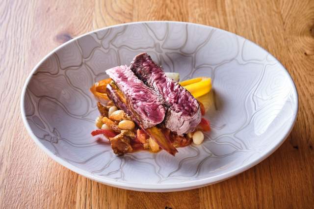 Pièce de viande rosée et légumes en sauce dans une assiette creuse texturée blanche – Boterzing Douai