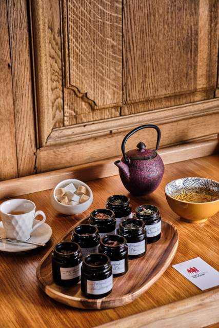 Théière en fonte violette et rangée de pots de thé sur plateau en bois naturel – La Table des Échevins Douai