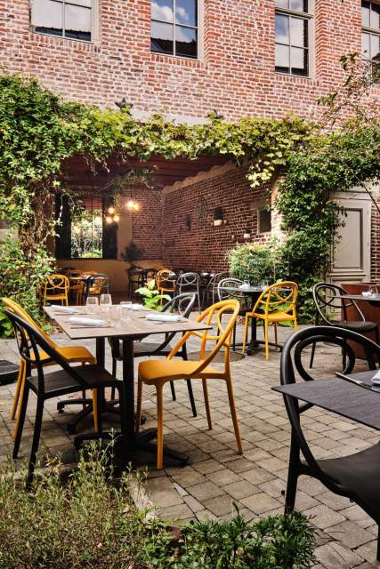 Terrasse intérieure avec chaises jaunes, murs en briques et végétation grimpante – Restaurant avec terrasse Douai